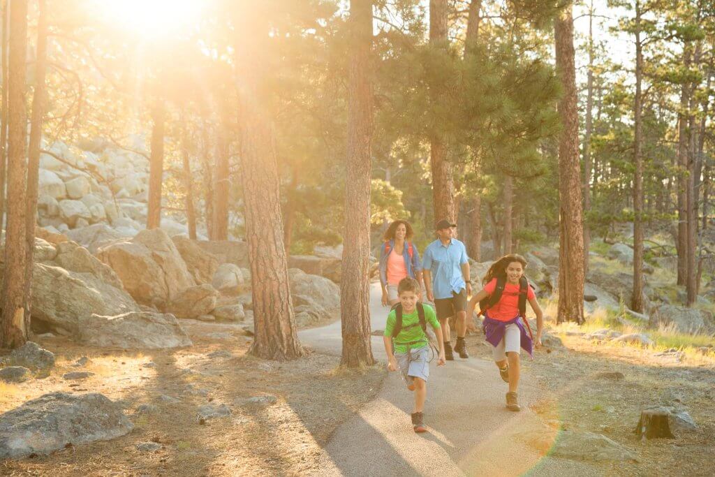 A happy family goes running on a hike as the sun streams through the Tower Trail by Devils Tower National Monument in Wyoming. 