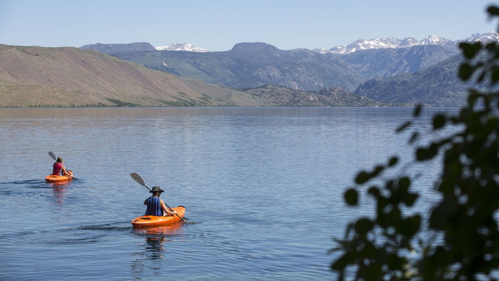 Two kayakers hold their oars as the water ripples across Fremont Lake in Pinedale, where snow-capped mountains tower in the distance.