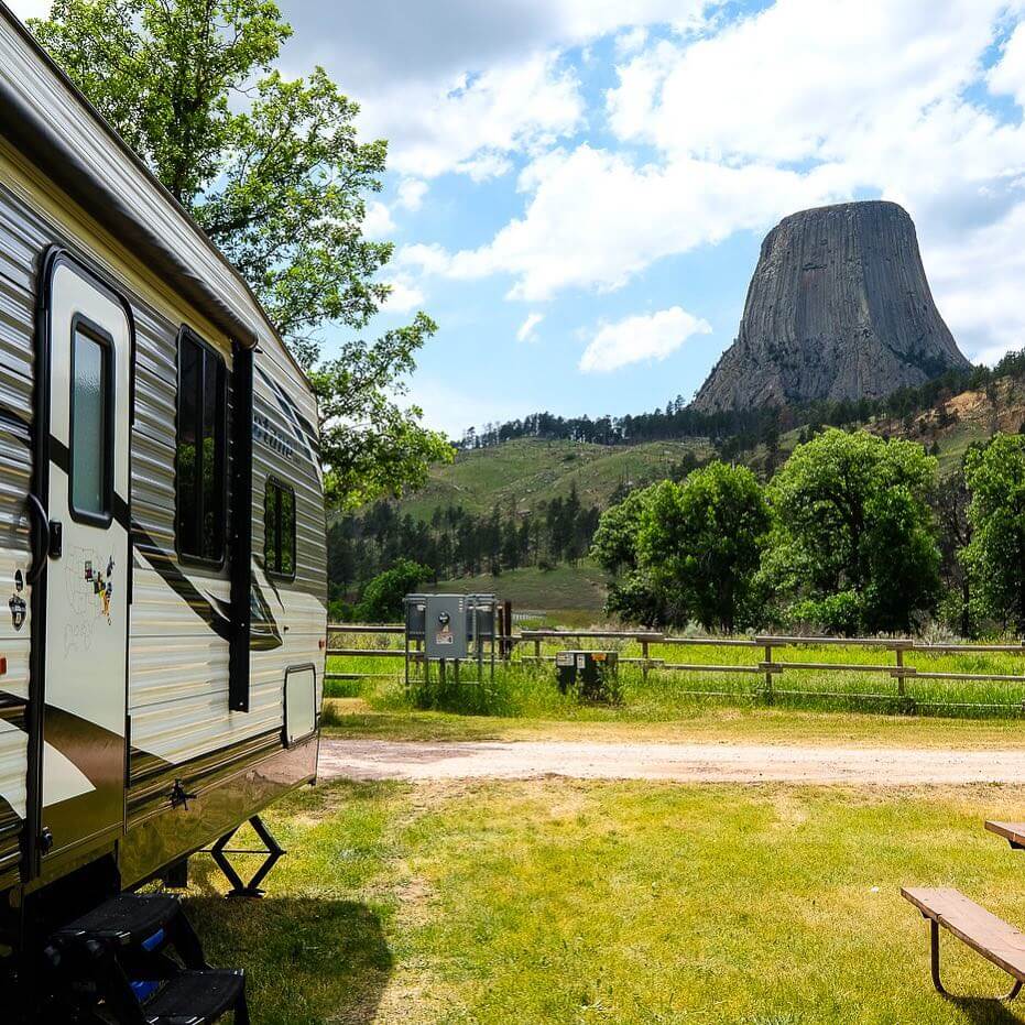 An RV camps outside before the green landscape leading up to Devils Tower National Monument.